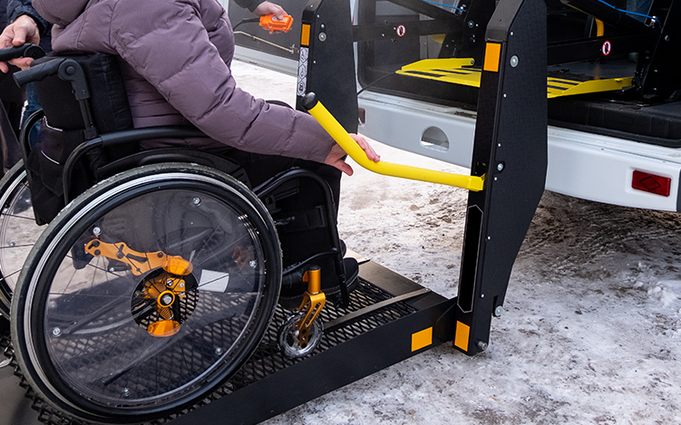Person in wheelchair being assisted by machine into vehicle